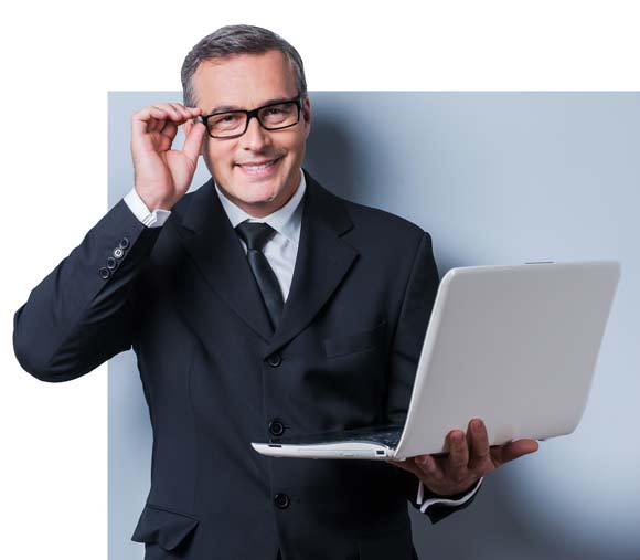 A man in a suit and glasses holding a laptop, looking focused and professional.
