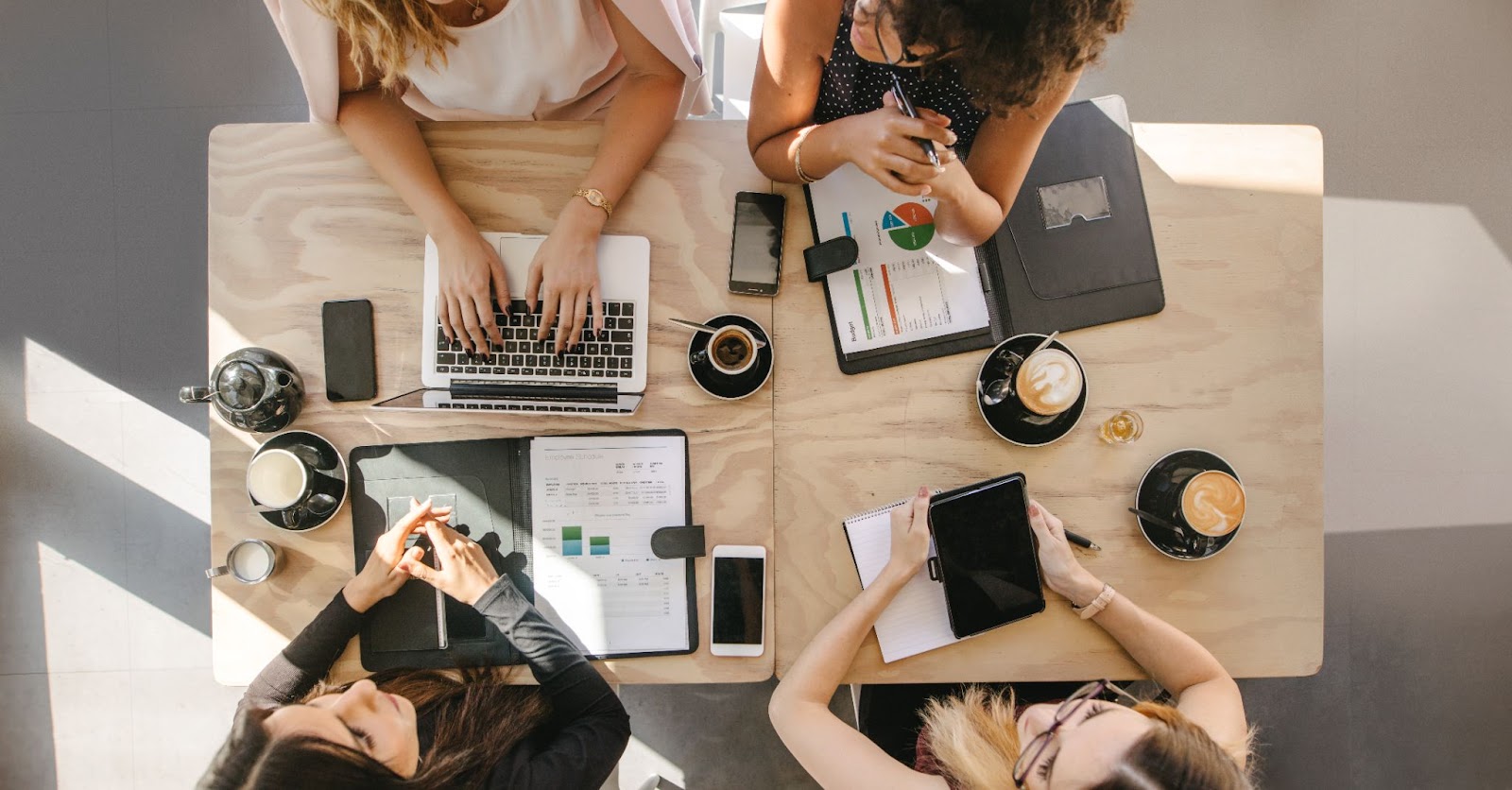 Three women collaborate at a table with laptops, discussing digital marketing strategies for their agency.