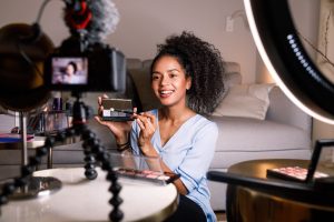 A woman holds a makeup mirror and camera, embodying the essence of influencer marketing and digital campaigns.