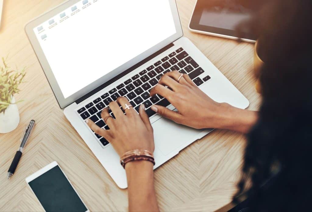 A woman focused on her laptop, preparing email subject lines for an email marketing agency, with a blank screen visible.