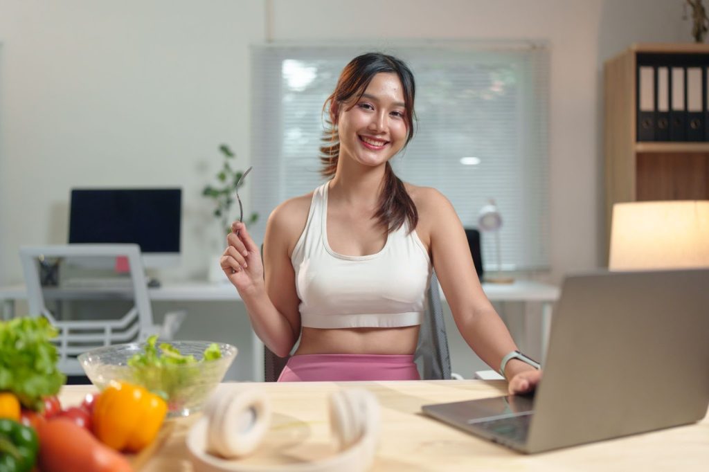 A woman in a sports bra sits at a table, focused on her laptop, representing a dynamic marketing environment in Utah.