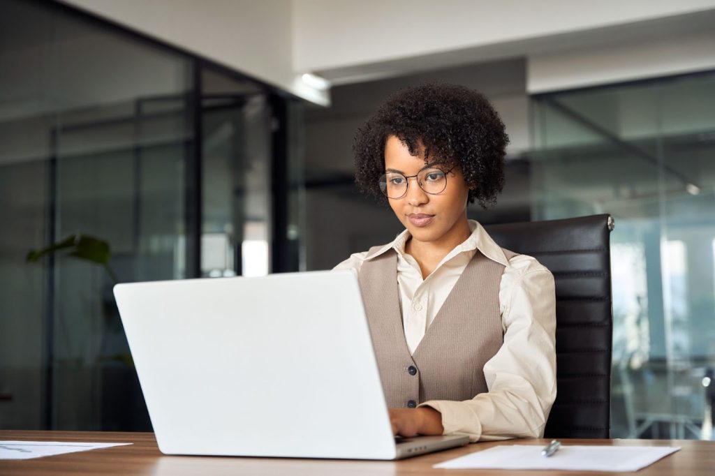 A woman wearing glasses sits at a desk, focused on her laptop, integrating AI into her marketing strategies.