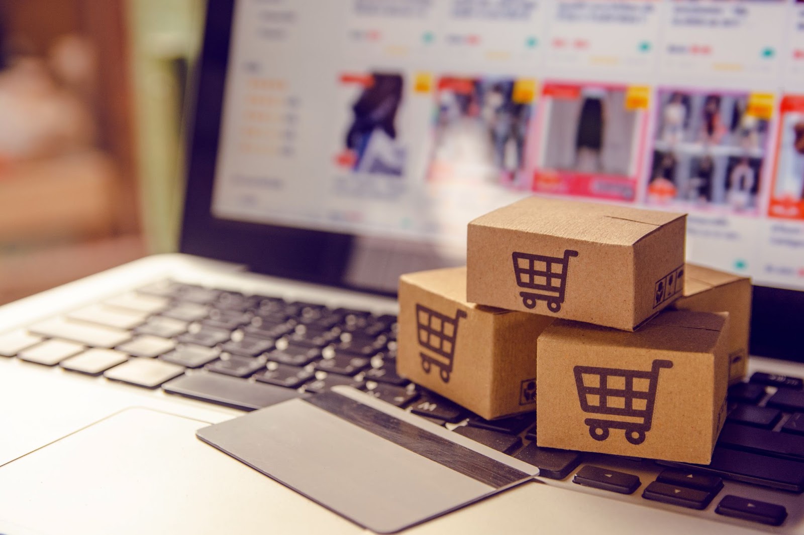 Laptop displaying an online shopping site with stacked boxes featuring shopping cart icons and a credit card.
