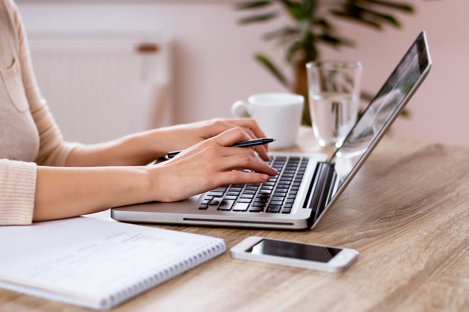 A woman types on her laptop at a desk, focused on her work in a well-lit environment.