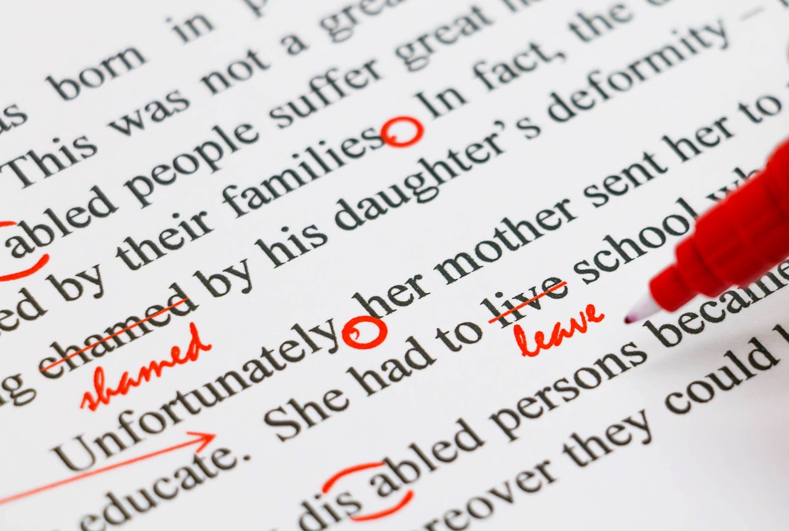 Close-up of a printed page with grammar corrections marked in red ink, showing circled words, crossed-out text, and handwritten edits.