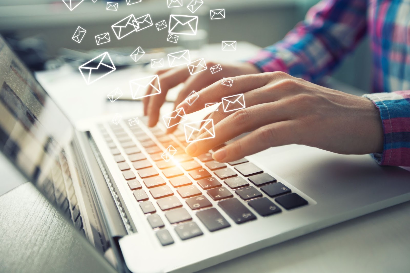 Close-up of hands typing on a laptop keyboard with digital email icons floating above it.
