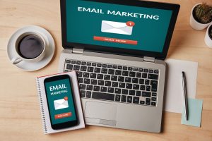 Top-down view of a laptop and smartphone on a desk, both displaying an Email Marketing notification.